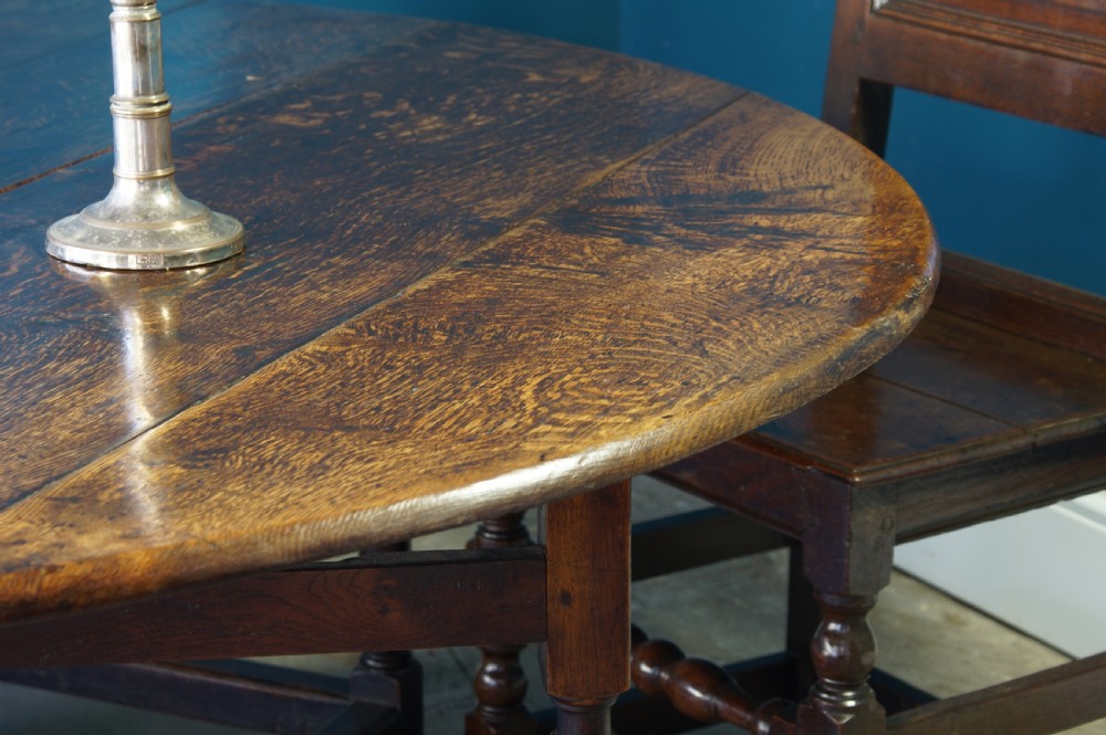 A large 18th-century dark oak gateleg dining table with a circular drop-leaf top supported by turned legs and stretchers. View XII