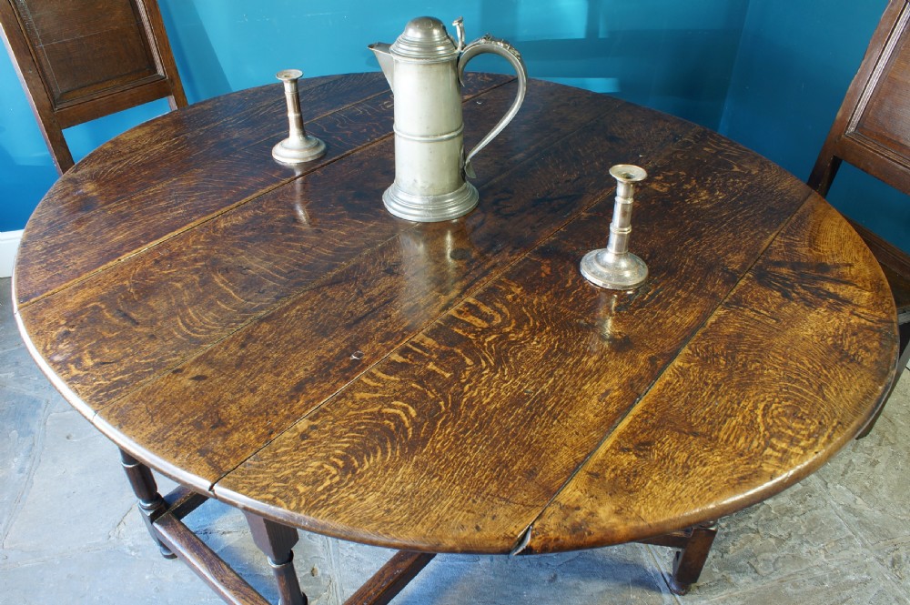 A large 18th-century dark oak gateleg dining table with a circular drop-leaf top supported by turned legs and stretchers. View XV
