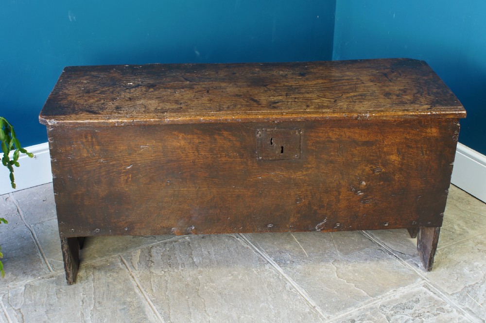 A dark brown 17th-century six-plank oak coffer featuring a flat top lid, iron lockplate, and bootjack side ends.
