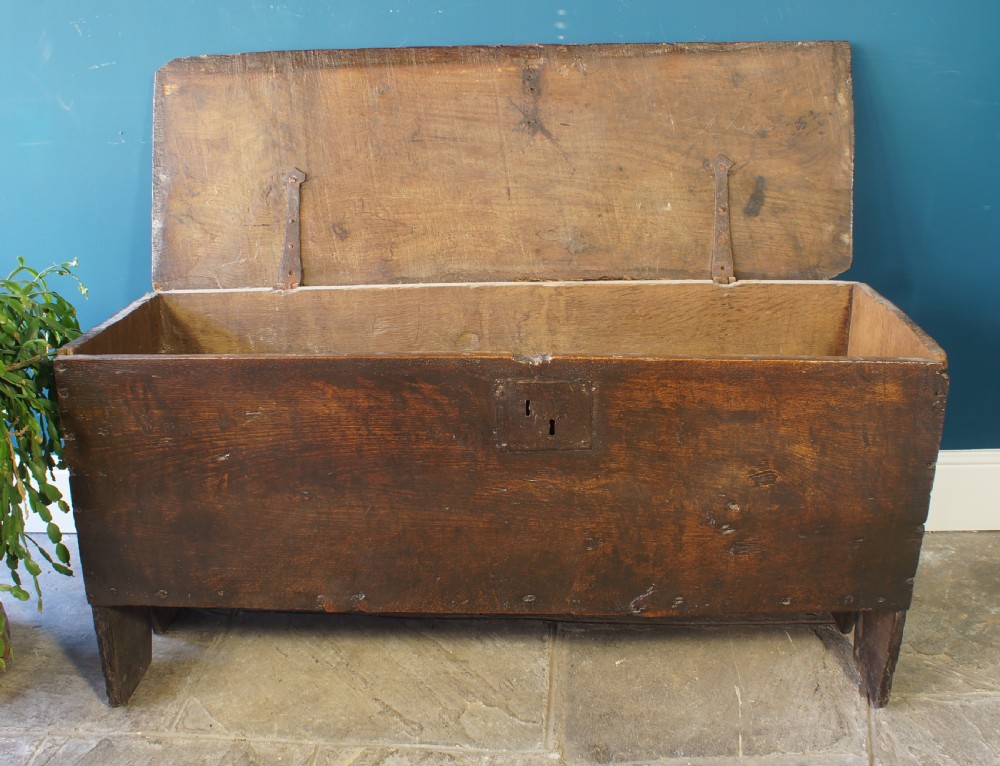 A dark brown 17th-century six-plank oak coffer featuring a flat top lid, iron lockplate, and bootjack side ends. View V