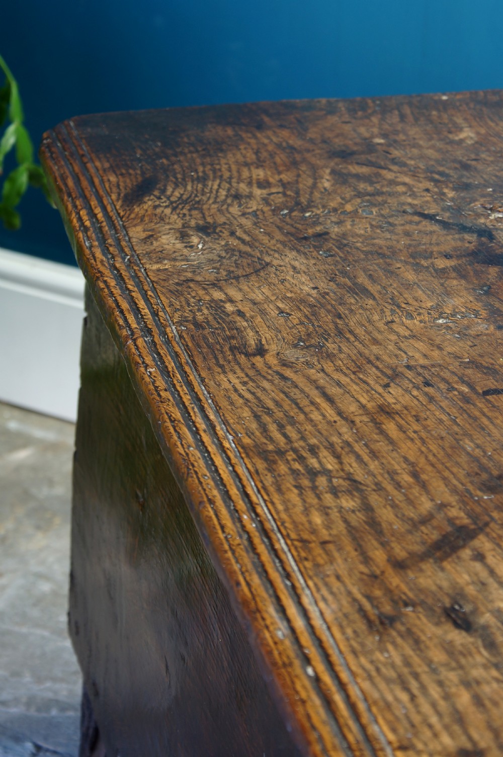 A dark brown 17th-century six-plank oak coffer featuring a flat top lid, iron lockplate, and bootjack side ends. View X