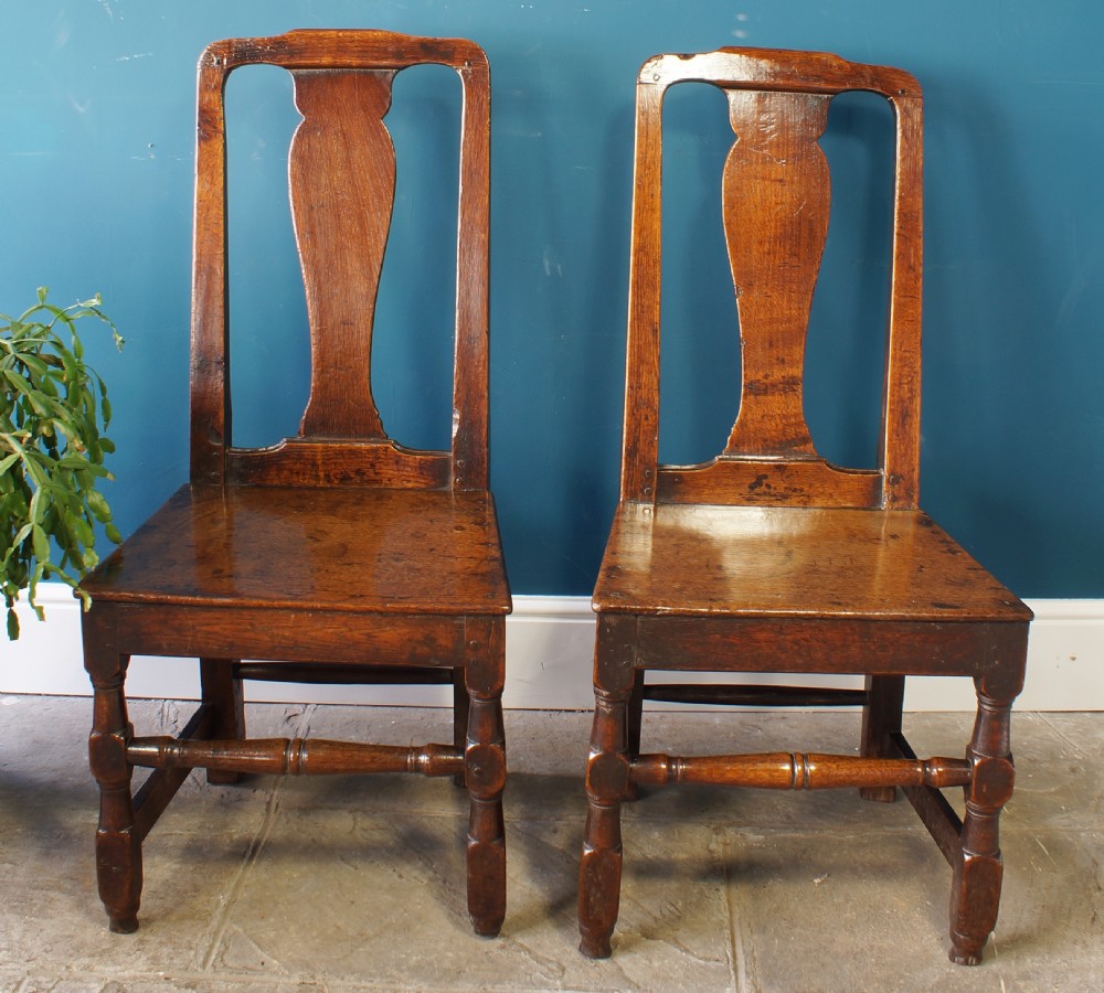 A pair of early 18th-century dark oak dining chairs with vase-shaped back splats, solid wooden seats, and turned front legs. View III
