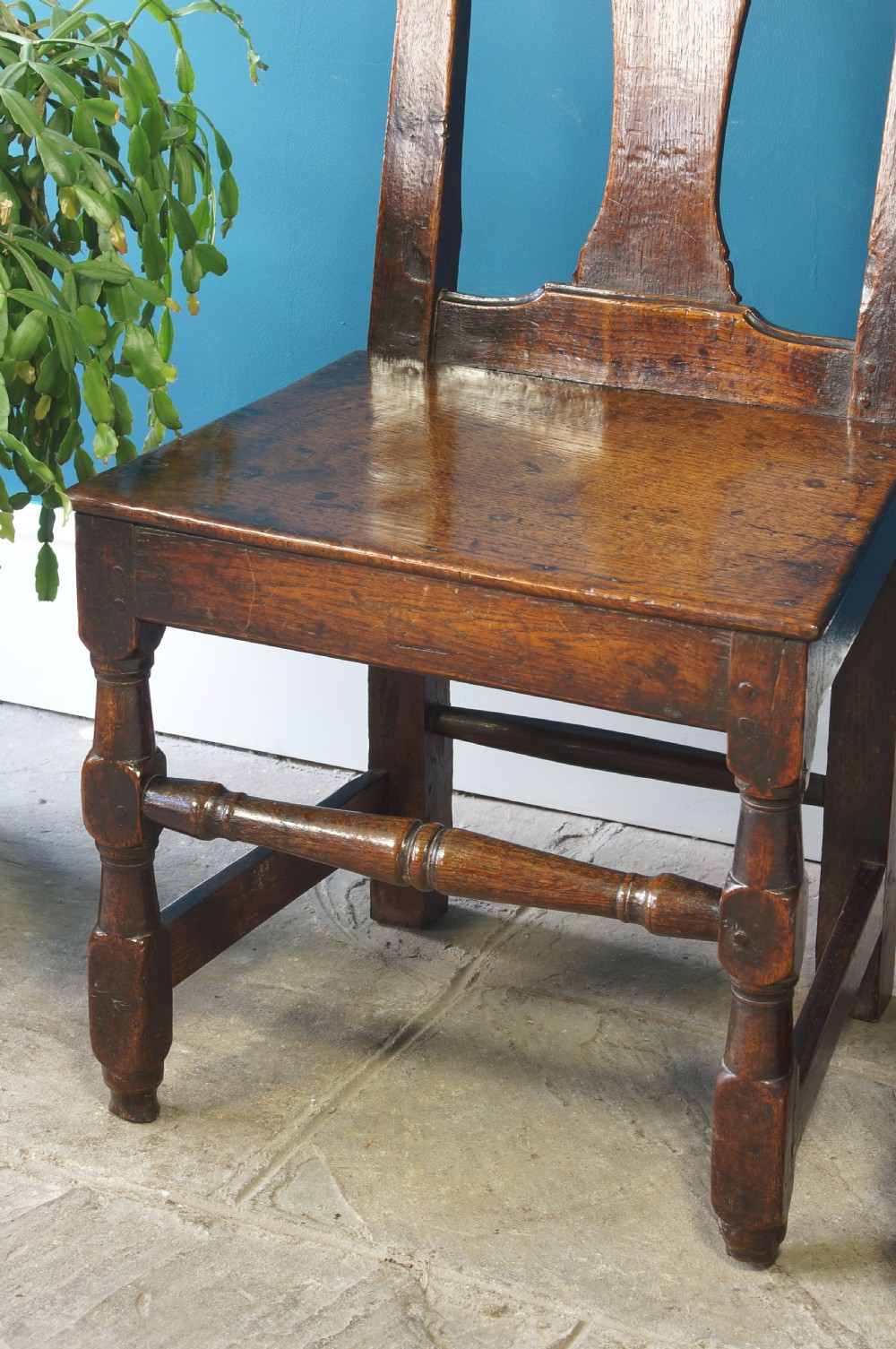 A pair of early 18th-century dark oak dining chairs with vase-shaped back splats, solid wooden seats, and turned front legs. View V