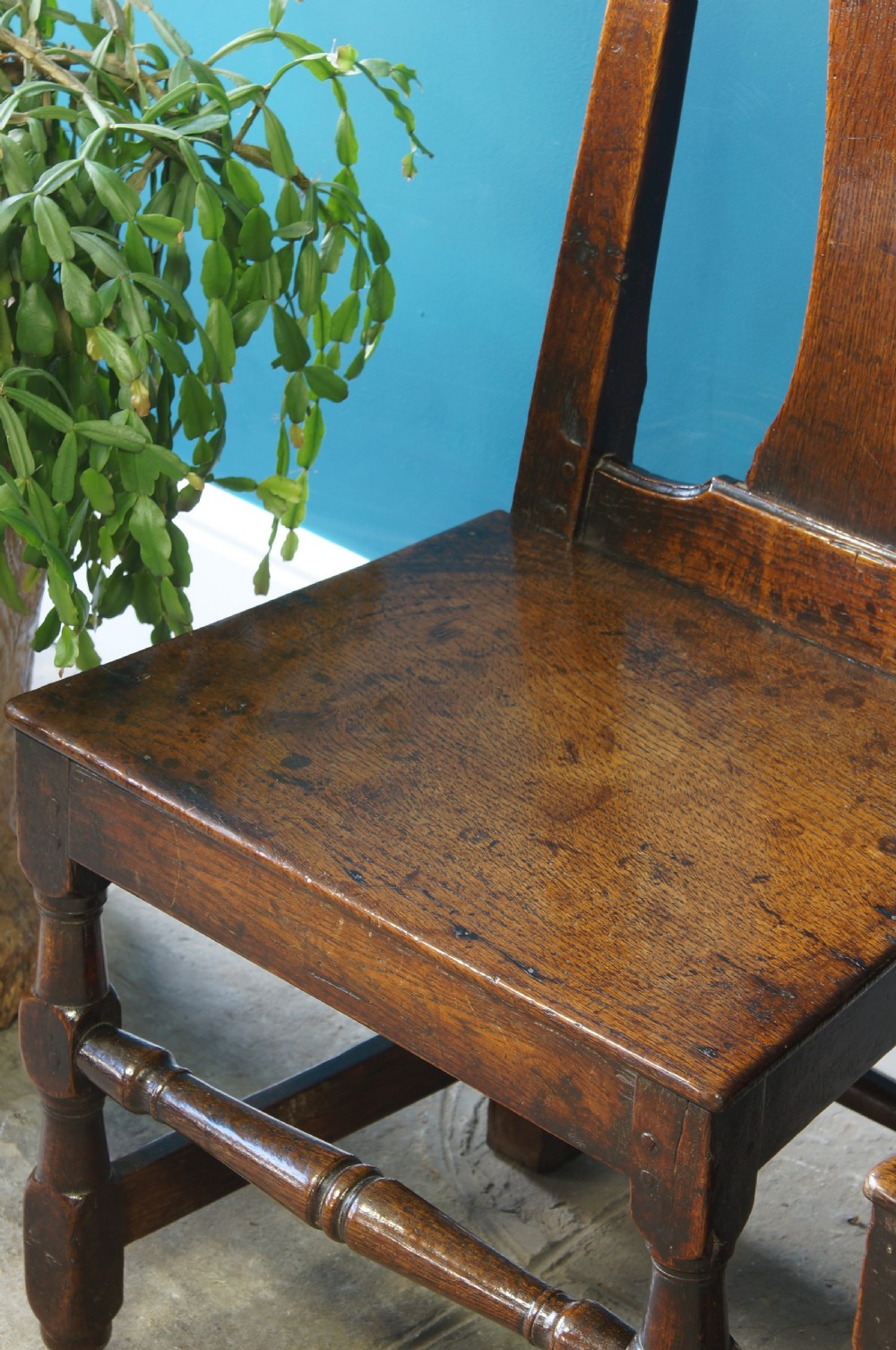 A pair of early 18th-century dark oak dining chairs with vase-shaped back splats, solid wooden seats, and turned front legs. View VI