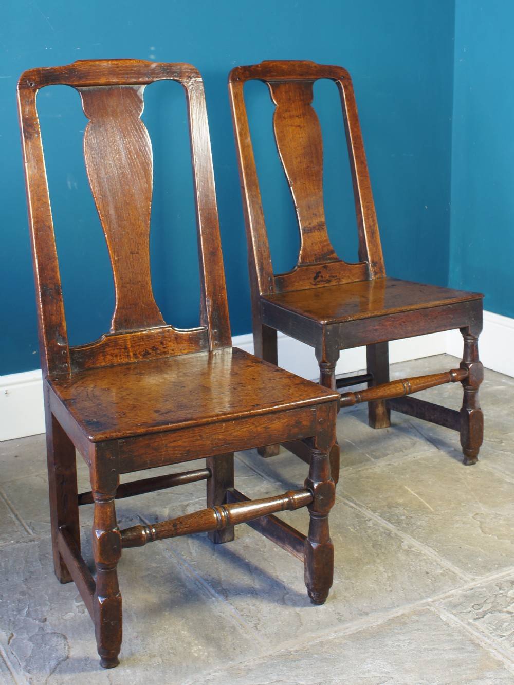 A pair of early 18th-century dark oak dining chairs with vase-shaped back splats, solid wooden seats, and turned front legs. View IX