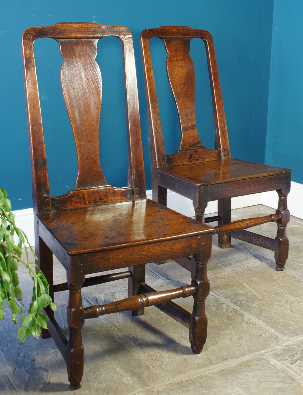 A pair of early 18th-century dark oak dining chairs with vase-shaped back splats, solid wooden seats, and turned front legs. View X