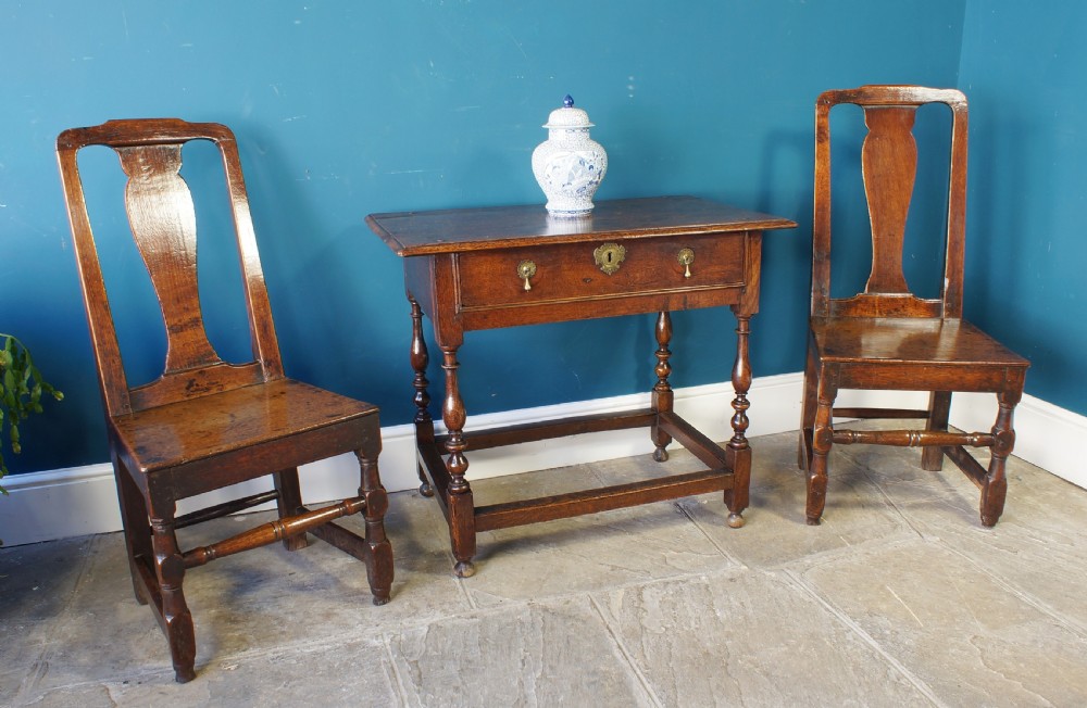 A pair of early 18th-century dark oak dining chairs with vase-shaped back splats, solid wooden seats, and turned front legs. View XI