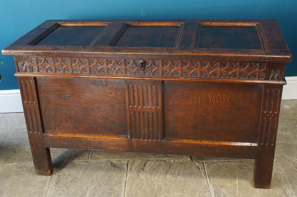 A 17th-century dark oak coffer with a carved geometric frieze, panelled front, and three-panel top lid.