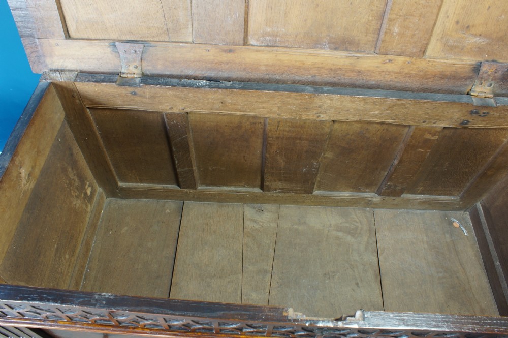 A 17th-century dark oak coffer with a carved geometric frieze, panelled front, and three-panel top lid. View V