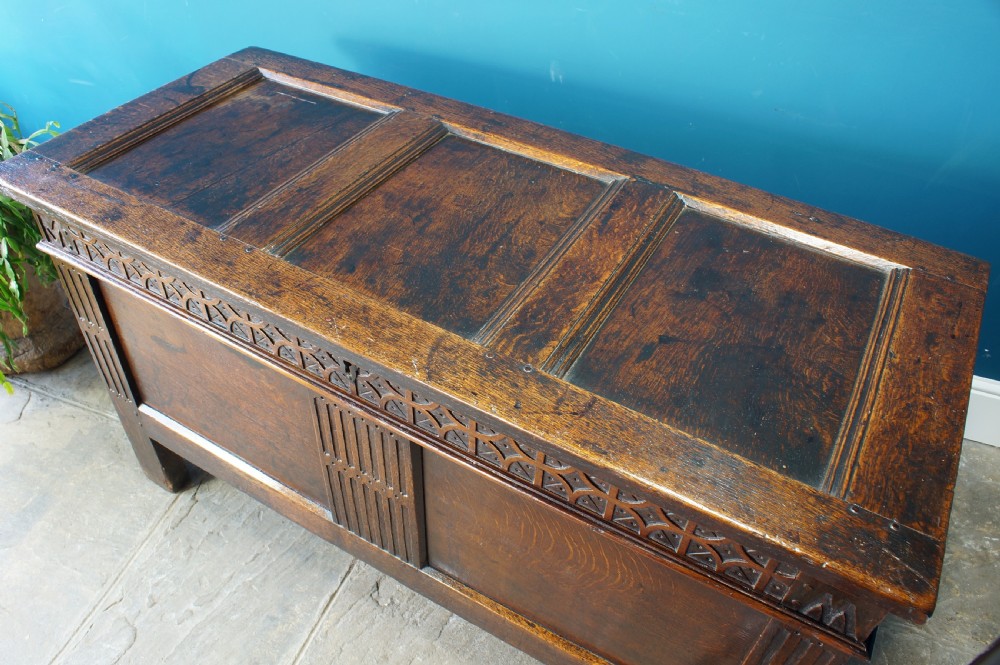 A 17th-century dark oak coffer with a carved geometric frieze, panelled front, and three-panel top lid. View VII