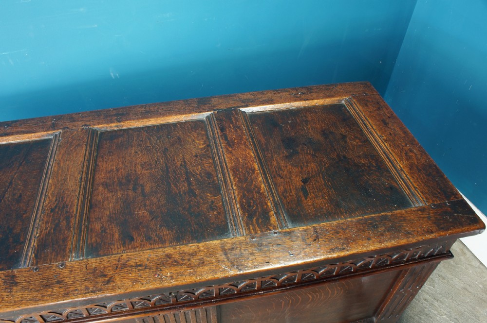A 17th-century dark oak coffer with a carved geometric frieze, panelled front, and three-panel top lid. View VIII