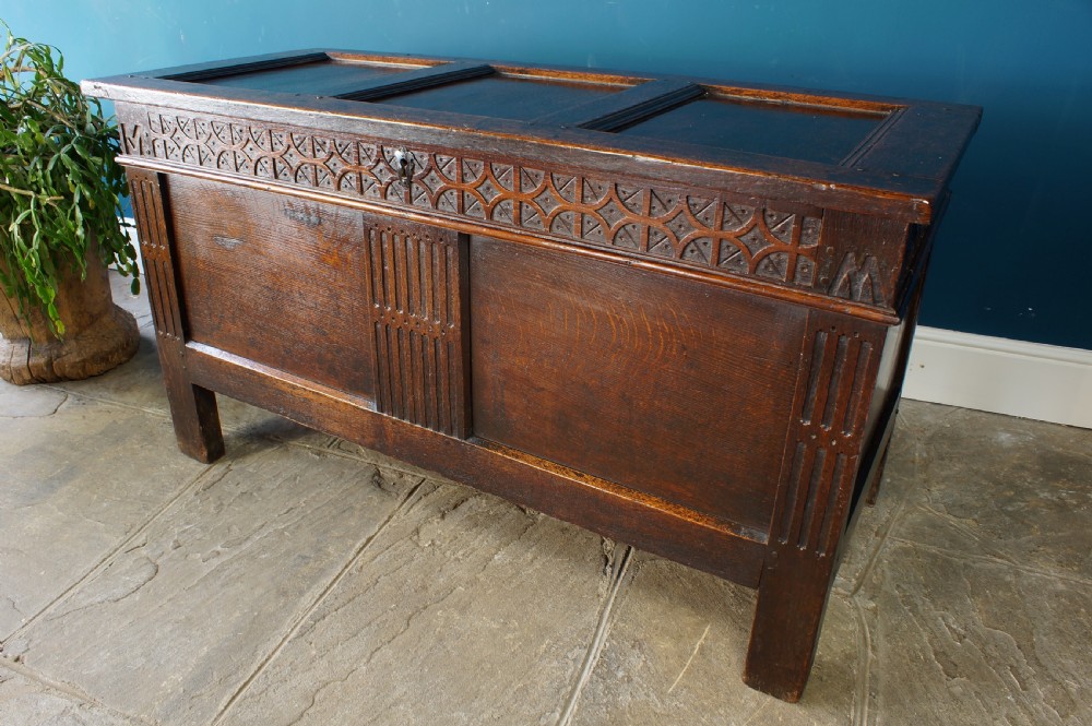 A 17th-century dark oak coffer with a carved geometric frieze, panelled front, and three-panel top lid. View IX