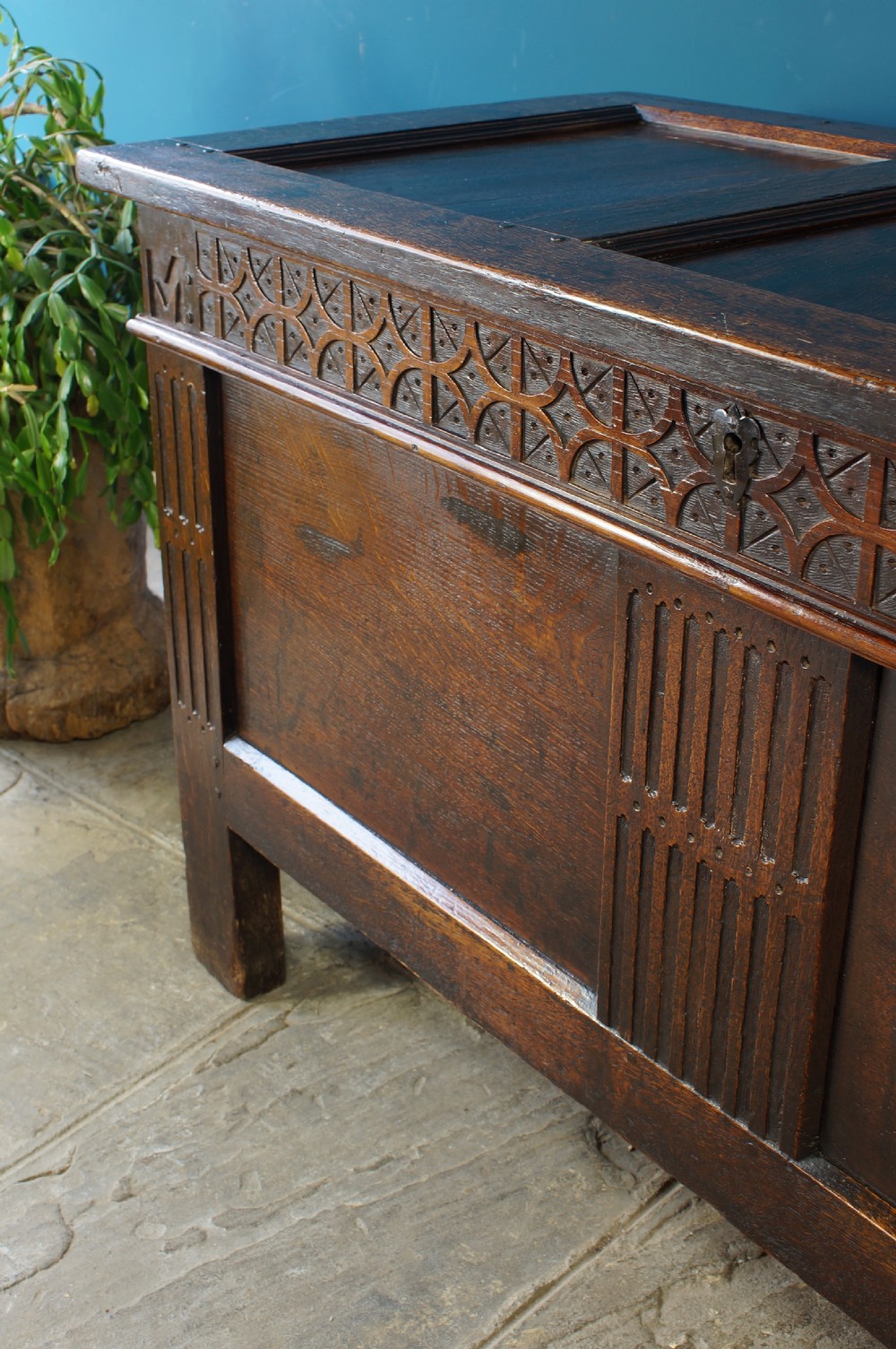A 17th-century dark oak coffer with a carved geometric frieze, panelled front, and three-panel top lid. View X