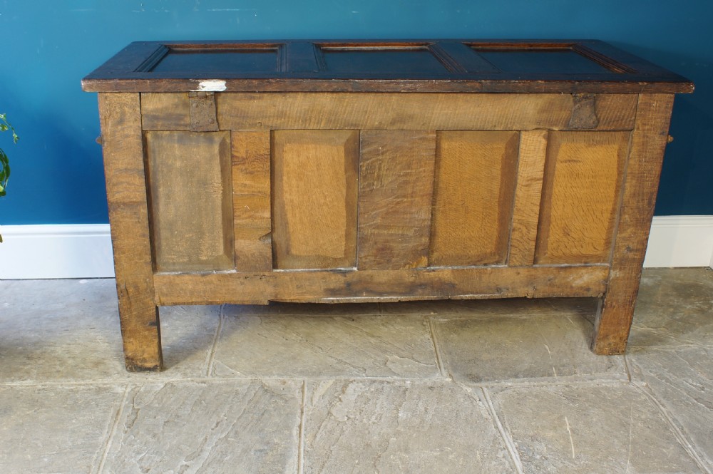 A 17th-century dark oak coffer with a carved geometric frieze, panelled front, and three-panel top lid. View XII