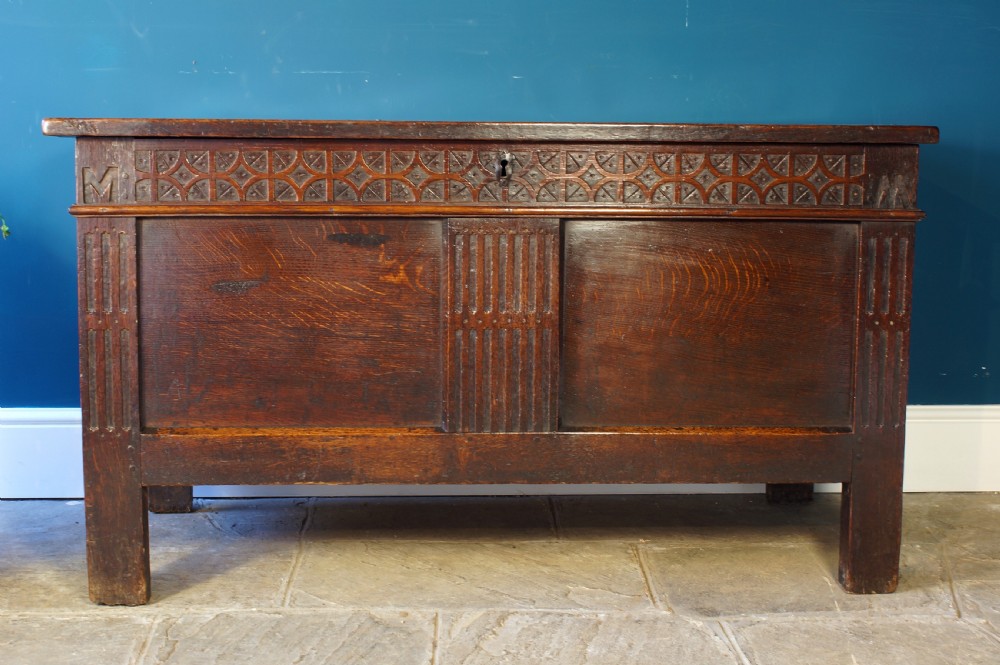 A 17th-century dark oak coffer with a carved geometric frieze, panelled front, and three-panel top lid. View XV