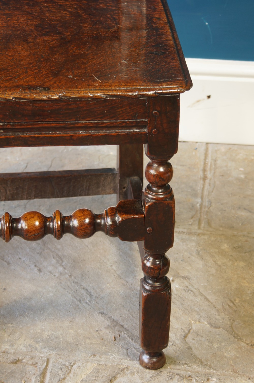 A dark oak 17th-century side chair with a carved floral back panel, solid plank seat, and bobbin-turned front stretcher. View III