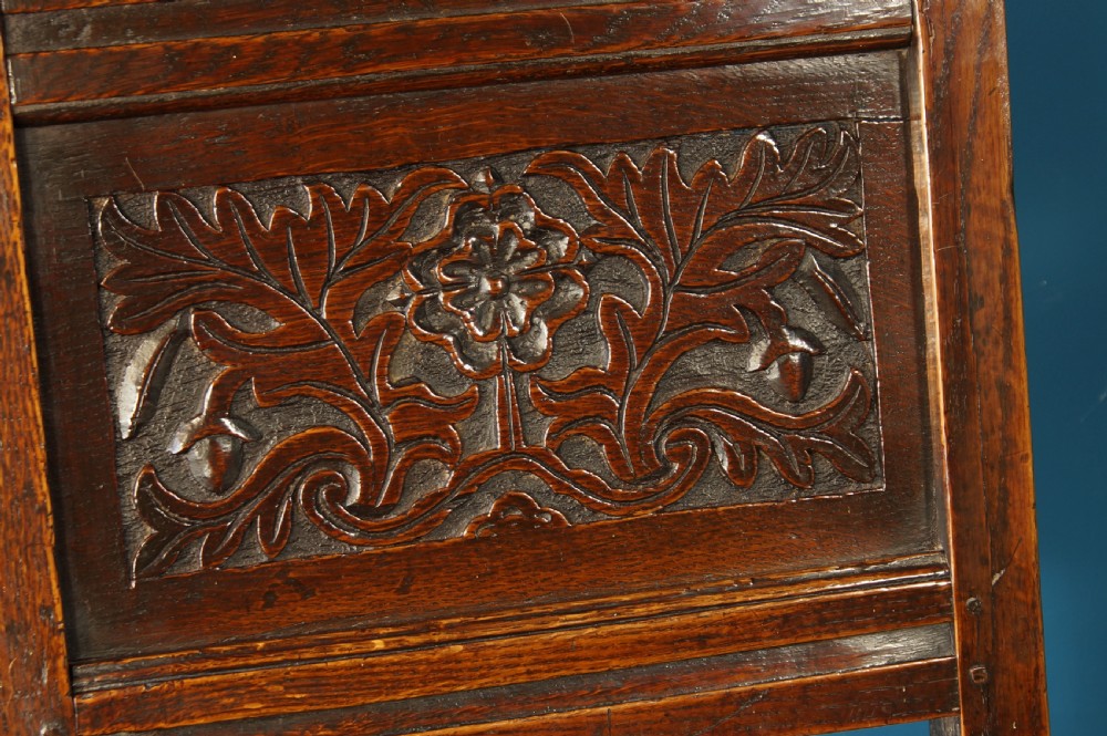 A dark oak 17th-century side chair with a carved floral back panel, solid plank seat, and bobbin-turned front stretcher. View IX