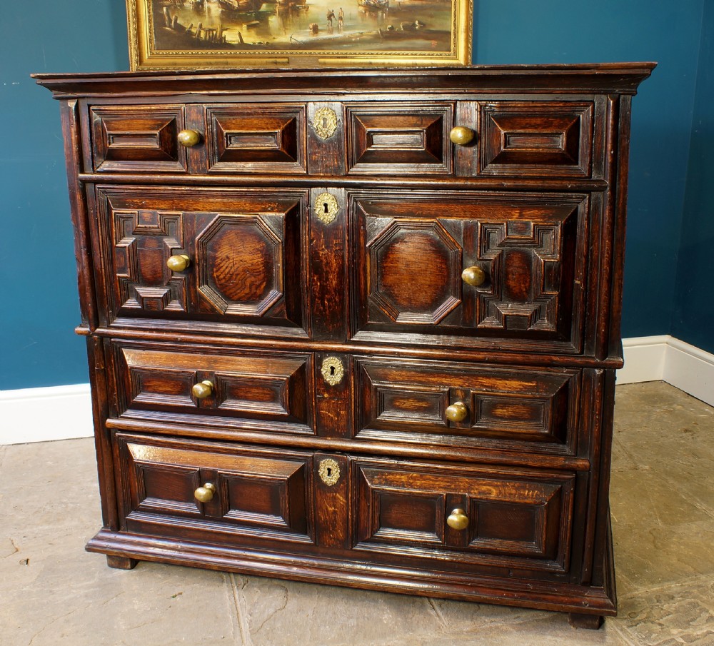 A dark oak 17th-century chest of drawers featuring geometric moulded drawer fronts and brass keyhole escutcheons.