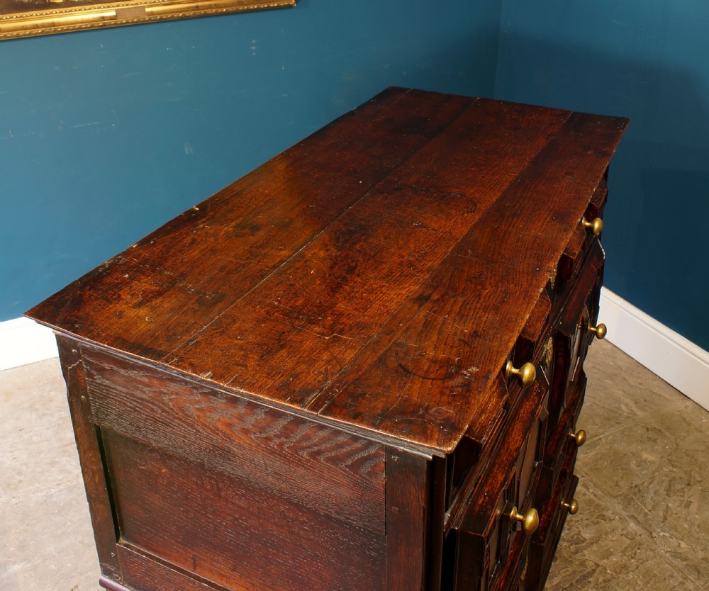 A dark oak 17th-century chest of drawers featuring geometric moulded drawer fronts and brass keyhole escutcheons. View VI