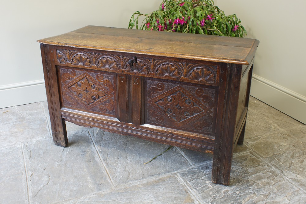 A small 17th-century dark oak coffer featuring hand-carved diamond panels, a decorative top frieze, and pegged joinery. View XII
