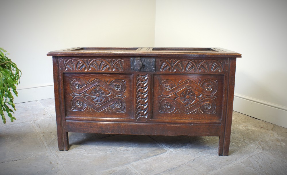 A 17th-century dark oak coffer featuring two carved front panels with geometric rosettes, an arcaded top rail, and an iron lockplate.