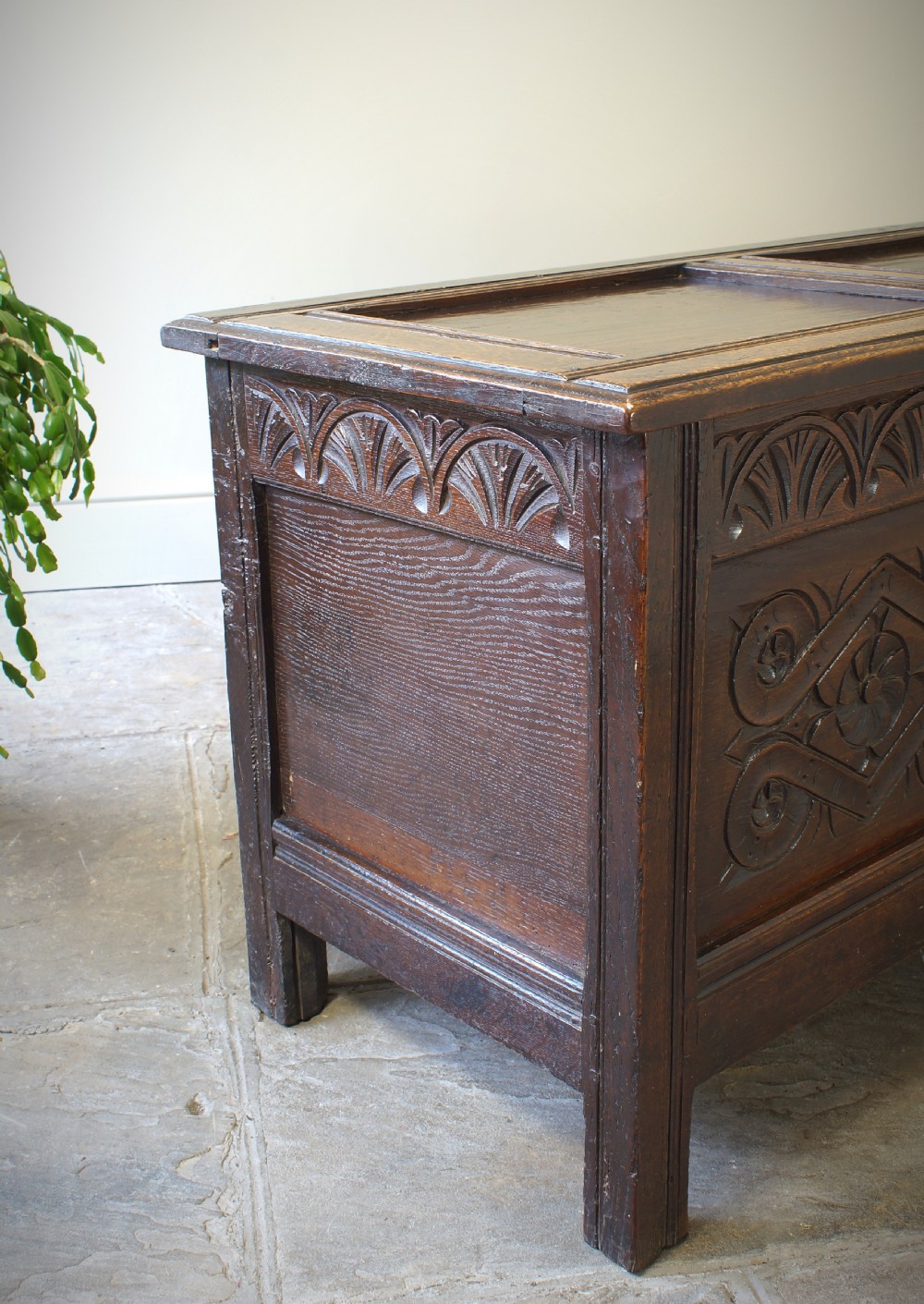 A 17th-century dark oak coffer featuring two carved front panels with geometric rosettes, an arcaded top rail, and an iron lockplate. View V
