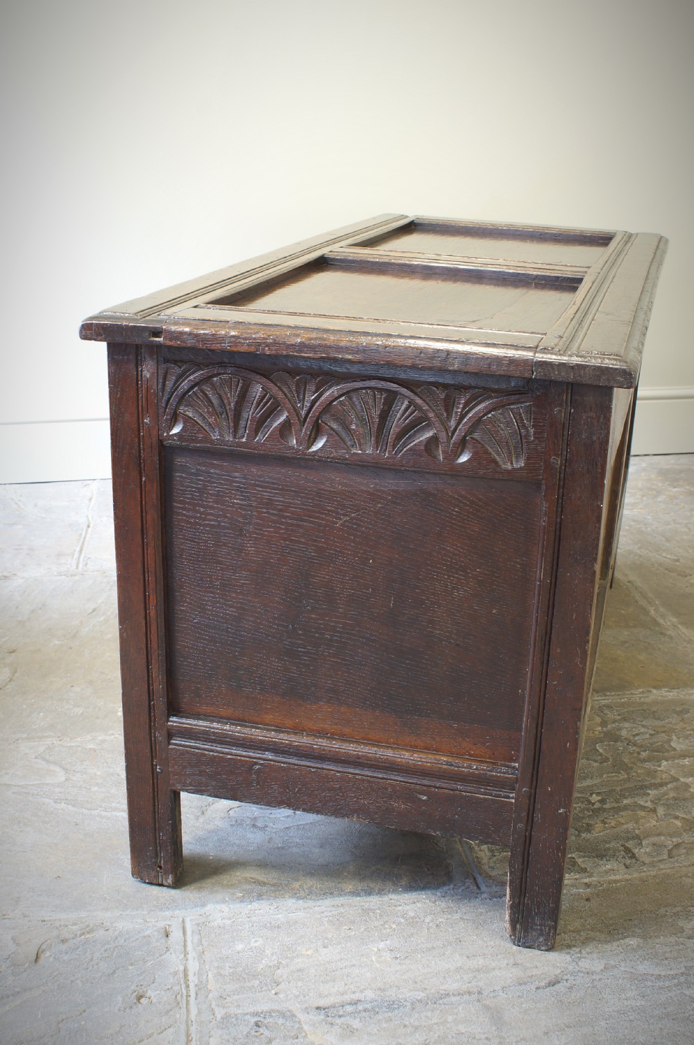 A 17th-century dark oak coffer featuring two carved front panels with geometric rosettes, an arcaded top rail, and an iron lockplate. View VI