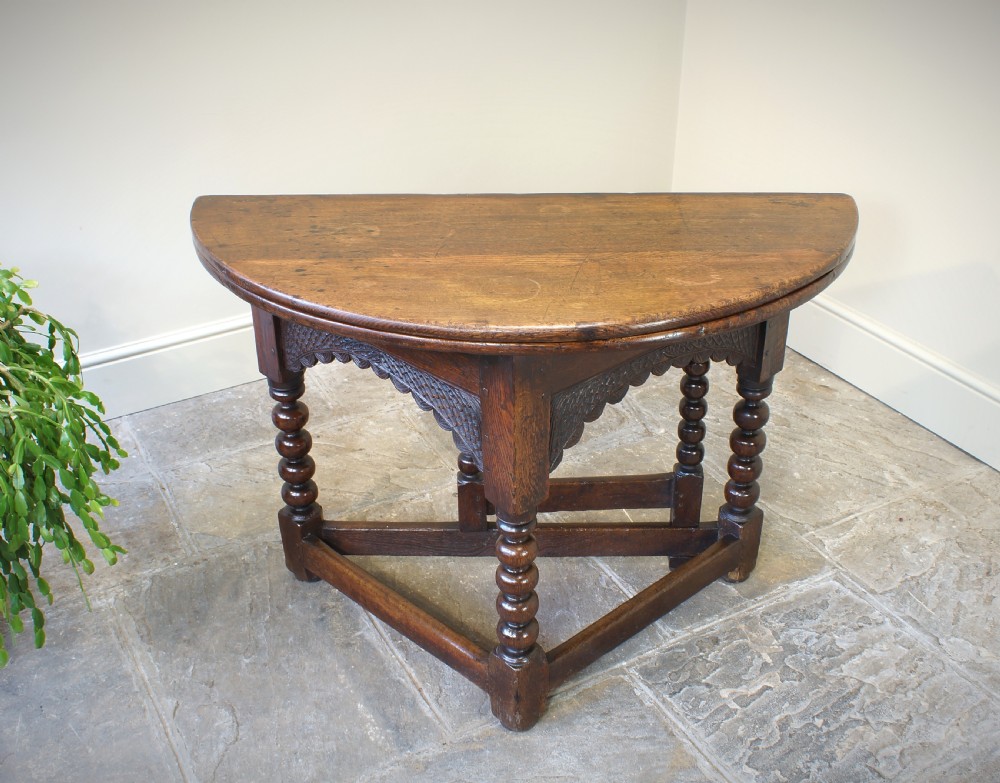 A 17th-century oak credence table featuring a semi-circular fold-over top, hand-carved frieze, turned legs, and low perimeter stretchers.