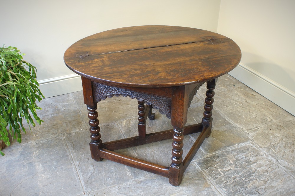 A 17th-century oak credence table featuring a semi-circular fold-over top, hand-carved frieze, turned legs, and low perimeter stretchers. View II