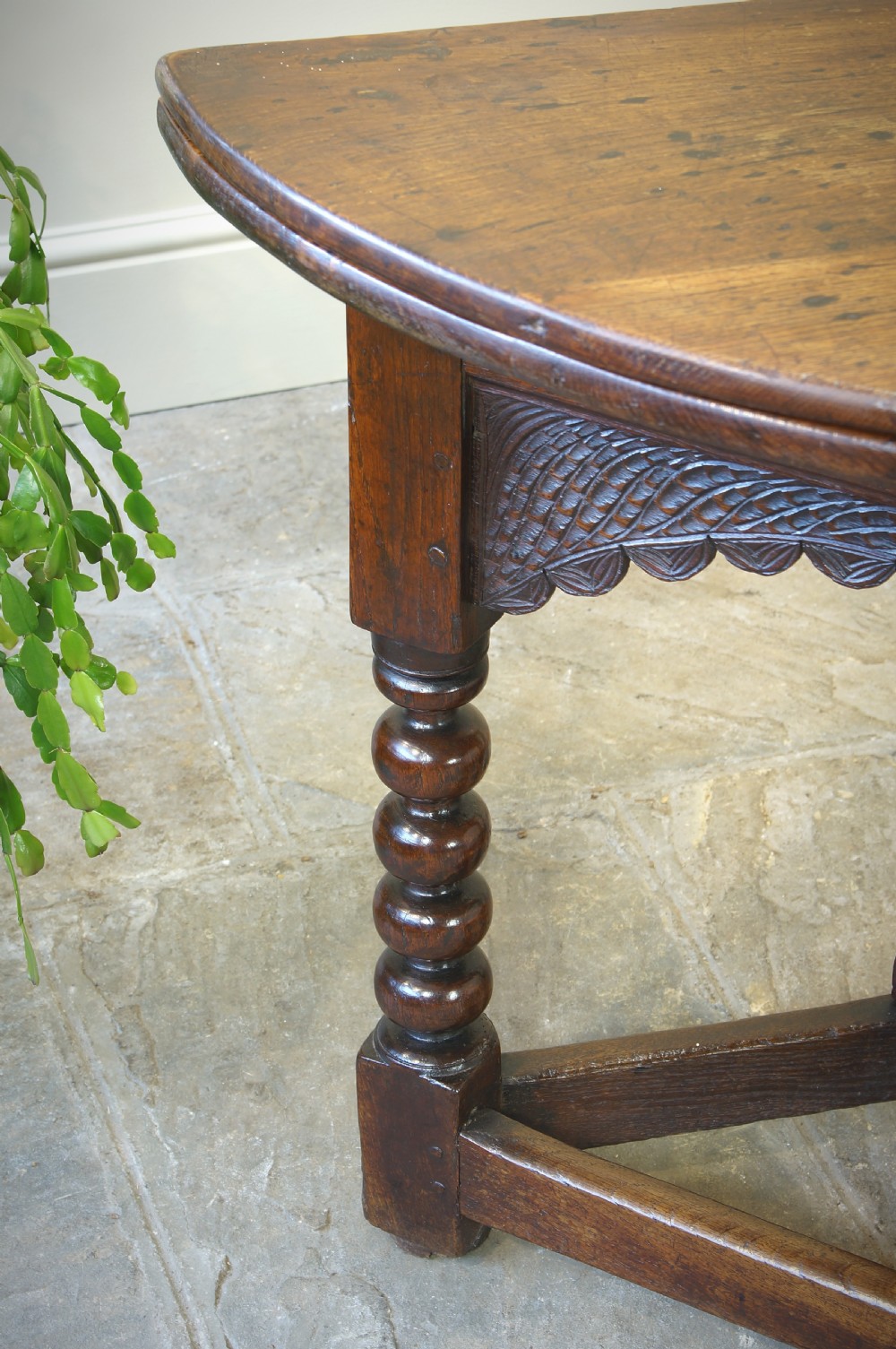 A 17th-century oak credence table featuring a semi-circular fold-over top, hand-carved frieze, turned legs, and low perimeter stretchers. View III