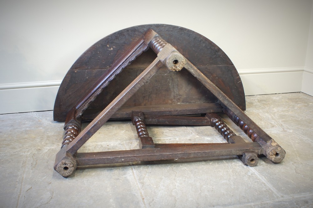A 17th-century oak credence table featuring a semi-circular fold-over top, hand-carved frieze, turned legs, and low perimeter stretchers. View VIII