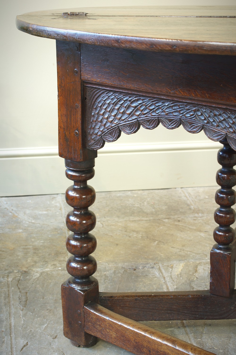 A 17th-century oak credence table featuring a semi-circular fold-over top, hand-carved frieze, turned legs, and low perimeter stretchers. View X