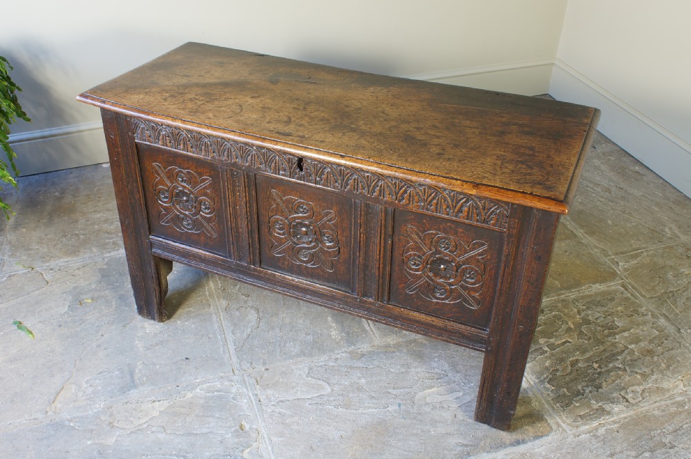 A small 17th-century dark oak coffer featuring three carved front panels, a carved top rail, and a hinged rectangular lid. View II