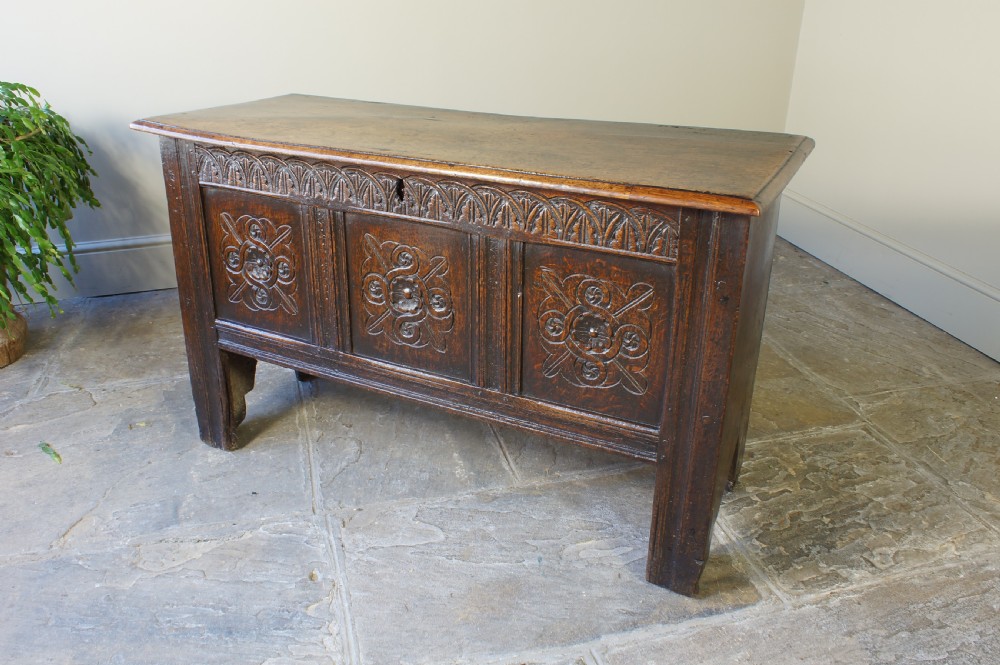 A small 17th-century dark oak coffer featuring three carved front panels, a carved top rail, and a hinged rectangular lid.