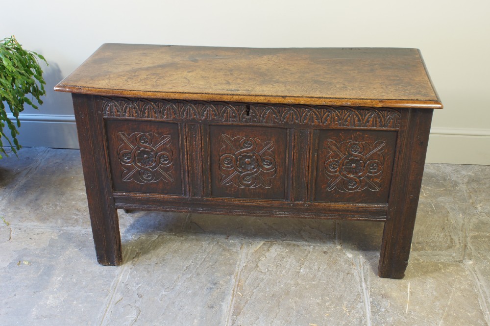 A small 17th-century dark oak coffer featuring three carved front panels, a carved top rail, and a hinged rectangular lid. View V