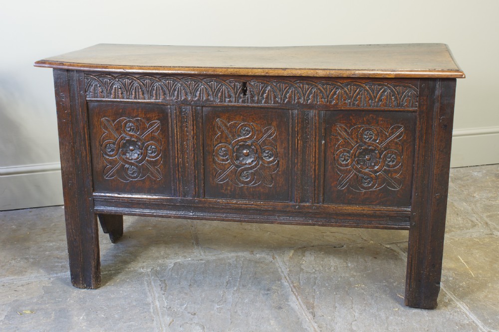 A small 17th-century dark oak coffer featuring three carved front panels, a carved top rail, and a hinged rectangular lid. View VII