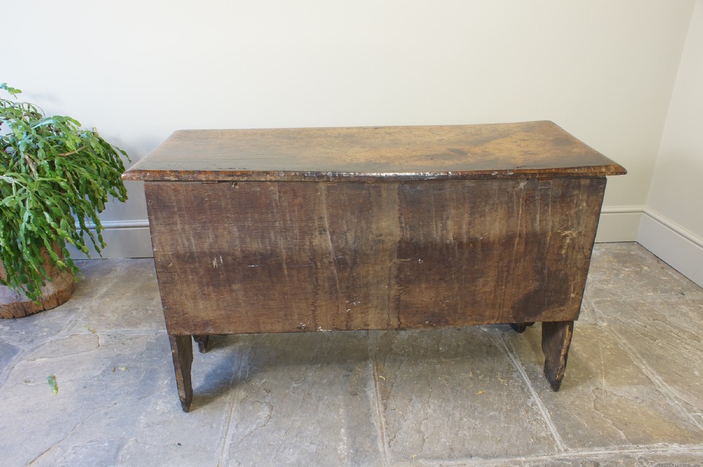 A small 17th-century dark oak coffer featuring three carved front panels, a carved top rail, and a hinged rectangular lid. View XI