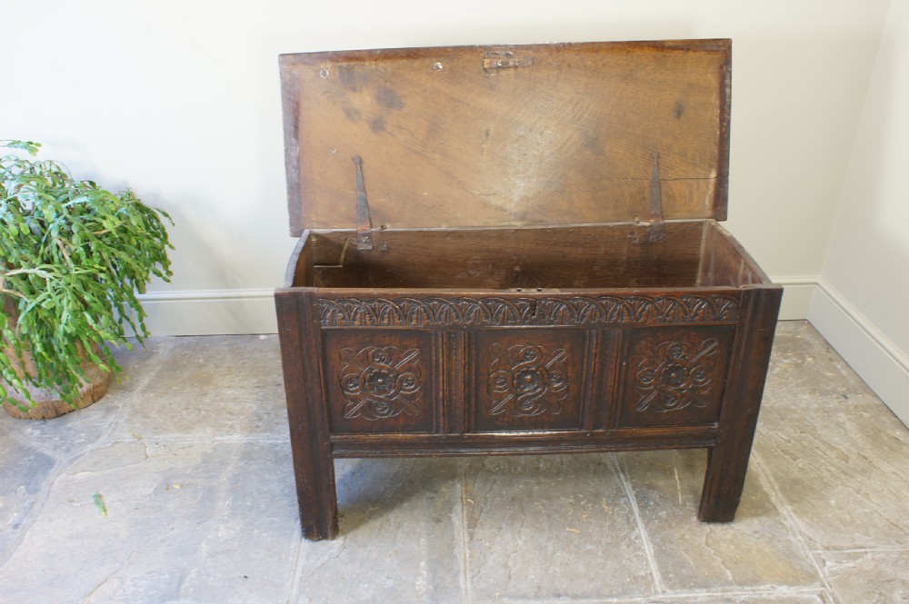 A small 17th-century dark oak coffer featuring three carved front panels, a carved top rail, and a hinged rectangular lid. View XII