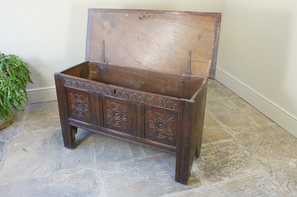 A small 17th-century dark oak coffer featuring three carved front panels, a carved top rail, and a hinged rectangular lid. View XIII