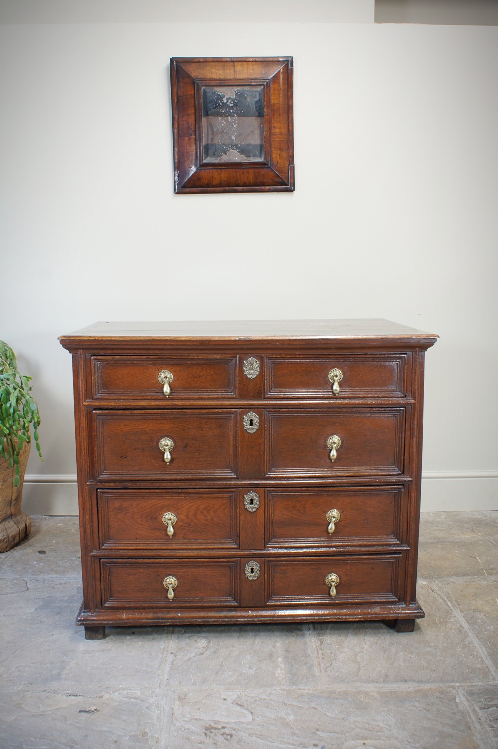 A seventeenth-century dark oak chest of drawers featuring geometric applied mouldings and brass teardrop handles.