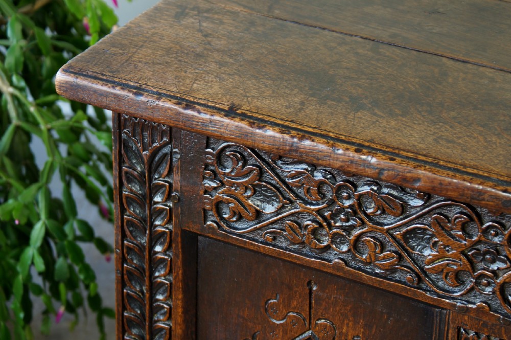A 17th-century carved dark oak coffer with four front panels featuring diamond motifs, a carved frieze, and a flat hinged lid. View V