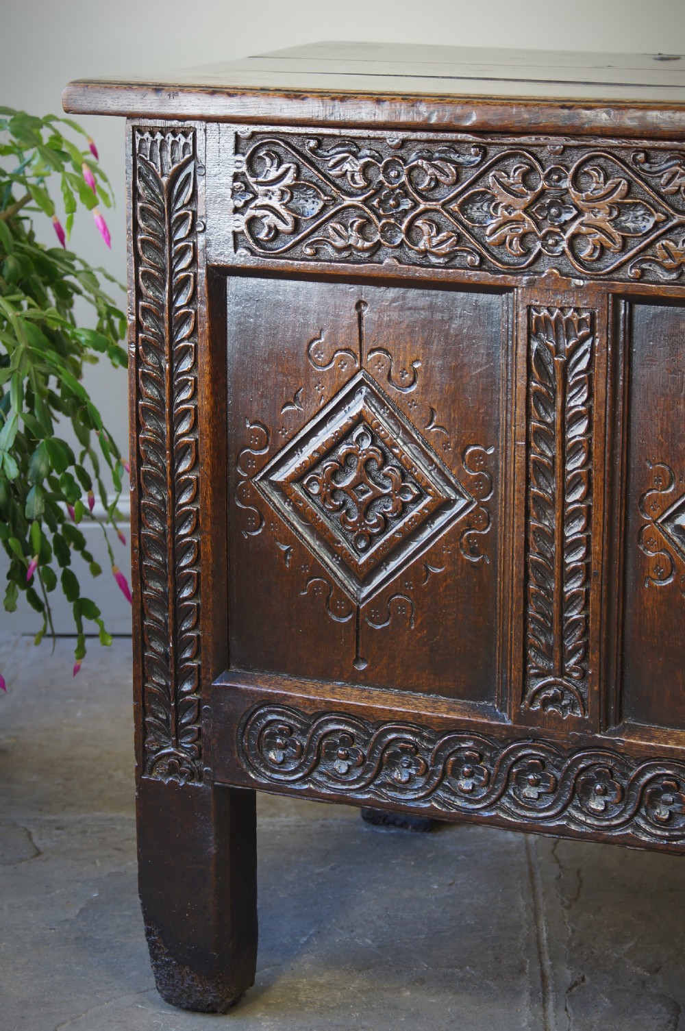 A 17th-century carved dark oak coffer with four front panels featuring diamond motifs, a carved frieze, and a flat hinged lid. View VI