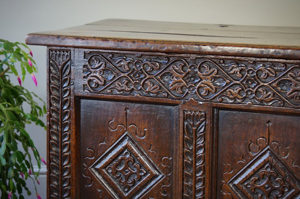 A 17th-century carved dark oak coffer with four front panels featuring diamond motifs, a carved frieze, and a flat hinged lid. View VII