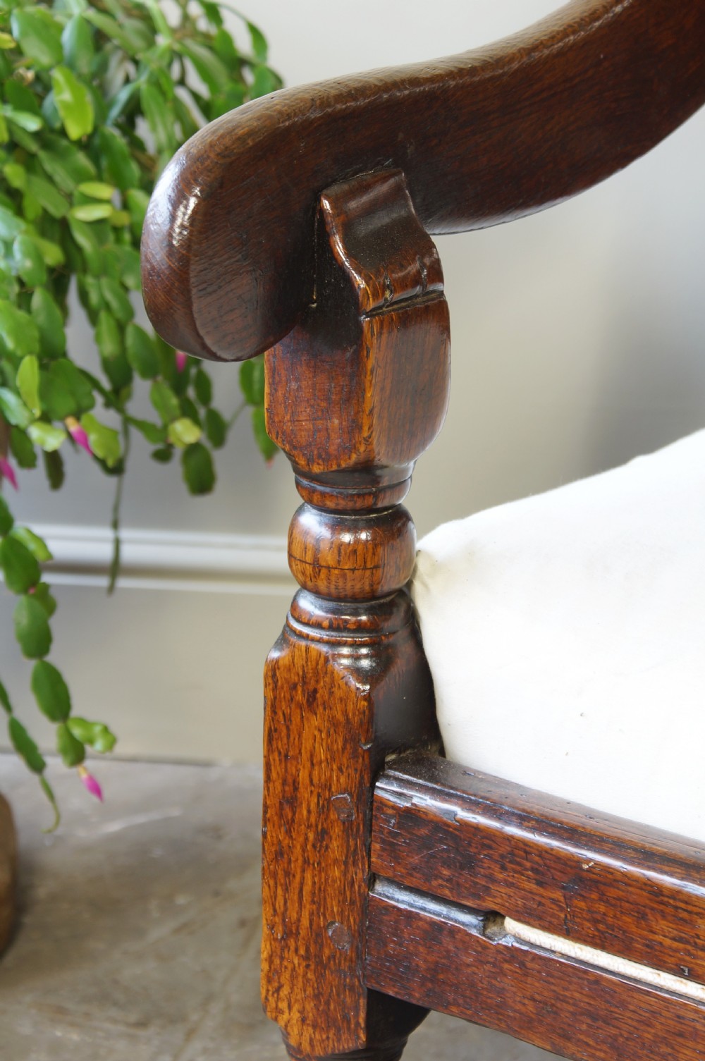 An early eighteenth-century dark oak settle featuring a five-panel shaped backrest, curved armrests, turned front legs, and a cream upholstered seat cushion. View VIII