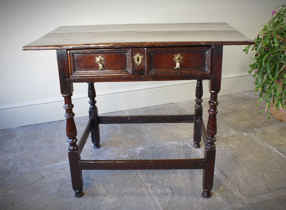 A late 17th-century dark oak side table featuring a single moulded drawer front, brass escutcheon, baluster-turned legs, and a perimeter box stretcher.