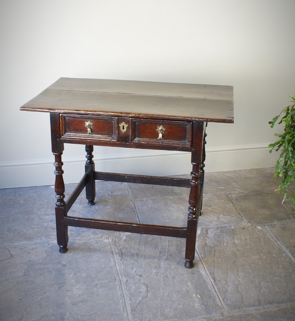 A late 17th-century dark oak side table featuring a single moulded drawer front, brass escutcheon, baluster-turned legs, and a perimeter box stretcher. View V