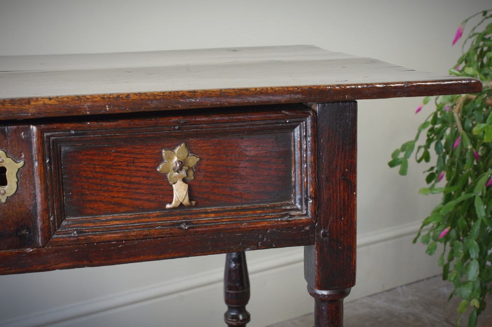 A late 17th-century dark oak side table featuring a single moulded drawer front, brass escutcheon, baluster-turned legs, and a perimeter box stretcher. View XIV