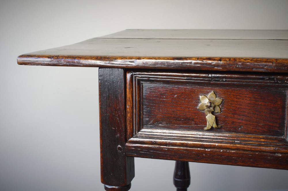 A late 17th-century dark oak side table featuring a single moulded drawer front, brass escutcheon, baluster-turned legs, and a perimeter box stretcher. View XV