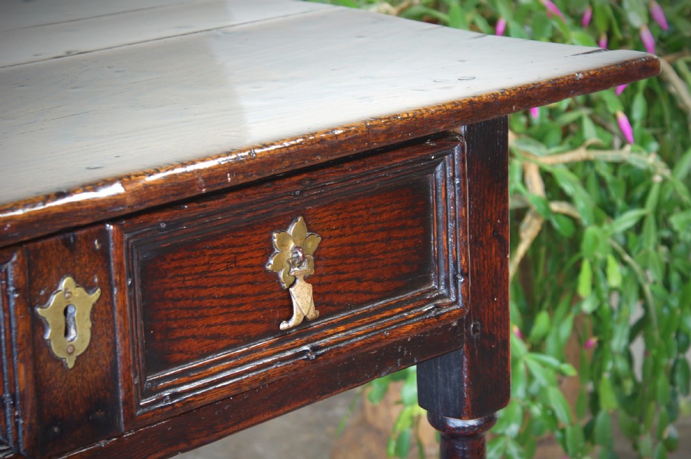 A late 17th-century dark oak side table featuring a single moulded drawer front, brass escutcheon, baluster-turned legs, and a perimeter box stretcher. View XVII