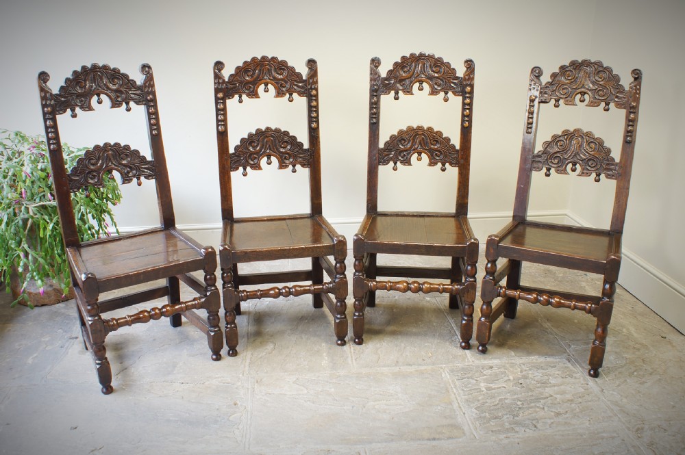 Set of four 17th-century carved dark oak backstool chairs featuring openwork carved cresting rails, turned stretchers, and solid wooden panel seats.